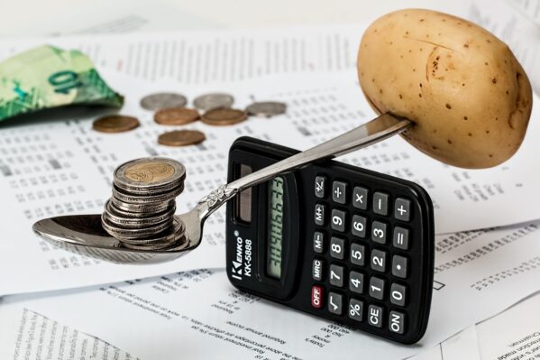 A calculator and a makeshift scale of a spoon, potato, and coins 