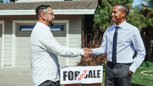 Two men shaking hands above the ’for sale’ sign