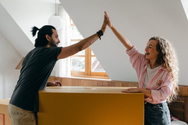 A man and a woman are excited and smiling next to a packed cardboard box.