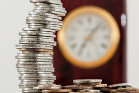 Stacked coins next to a wooden clock